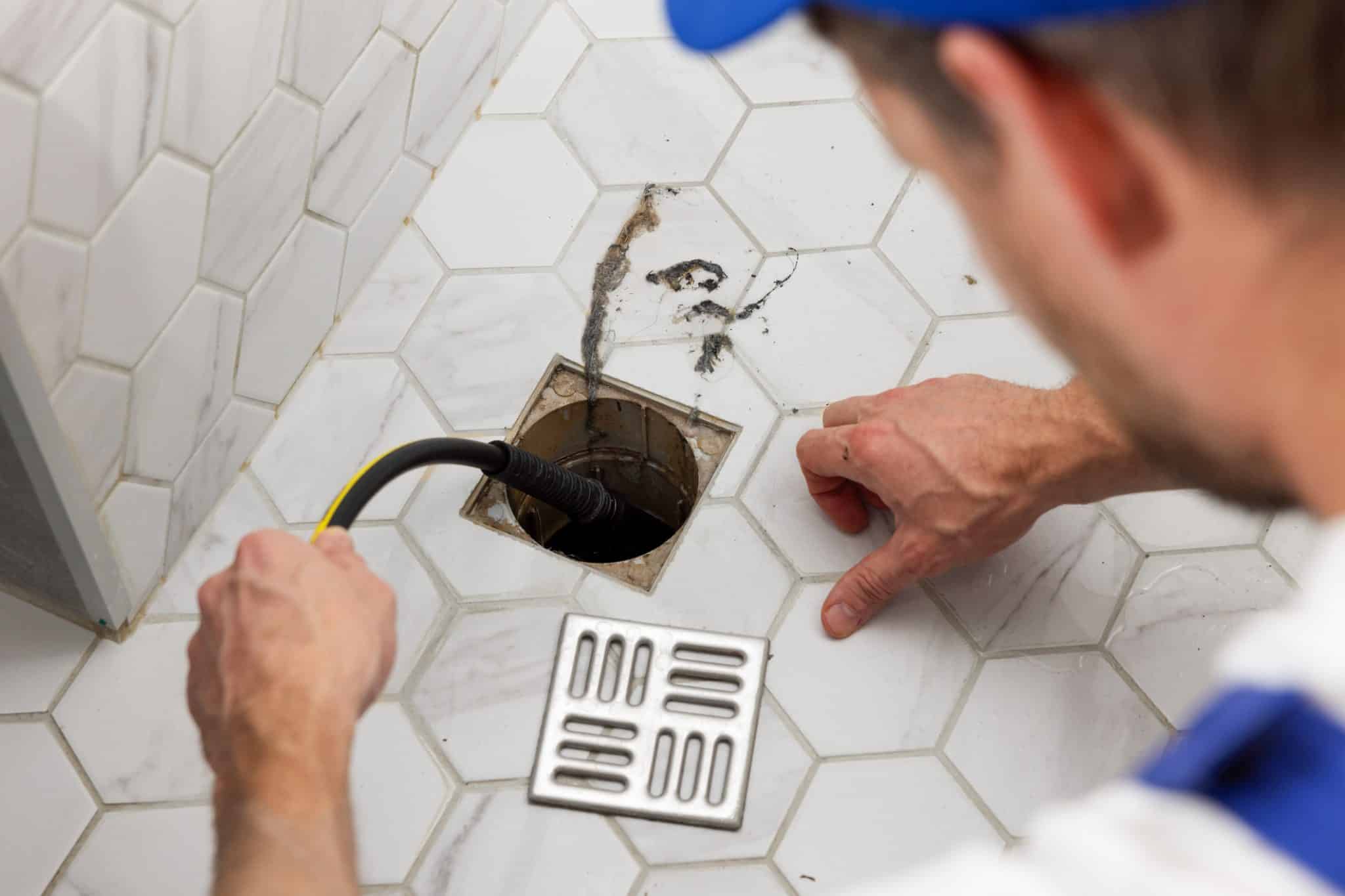 A professional administering drain cleaning services to a clogged shower drain.