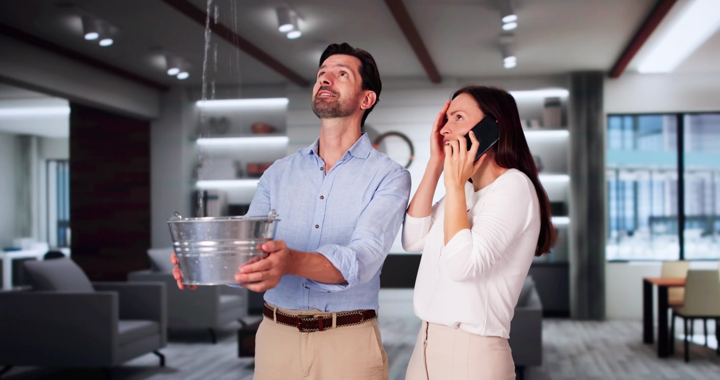 A couple catching leaking water from their ceiling with a bucket after DIY plumbing