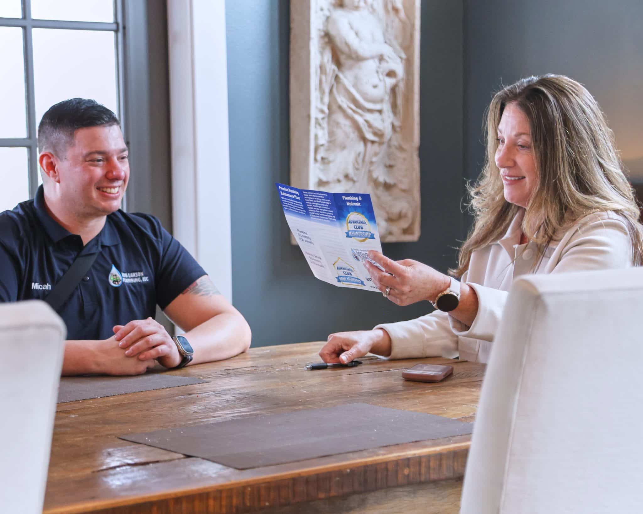 Bob Larson Plumbing technician explaining the plumbing membership program to a customer holding a membership brochure