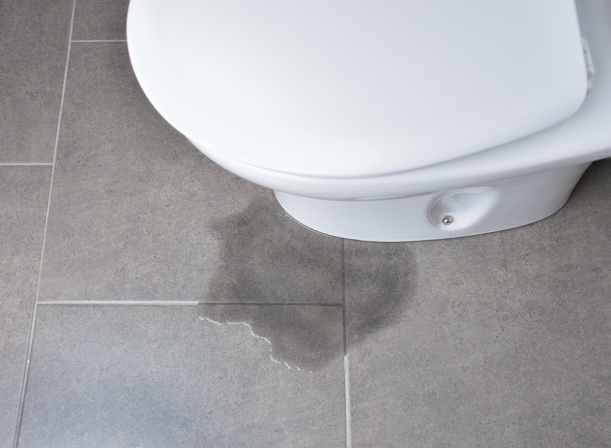 A toilet leaking from the base on a tile floor.